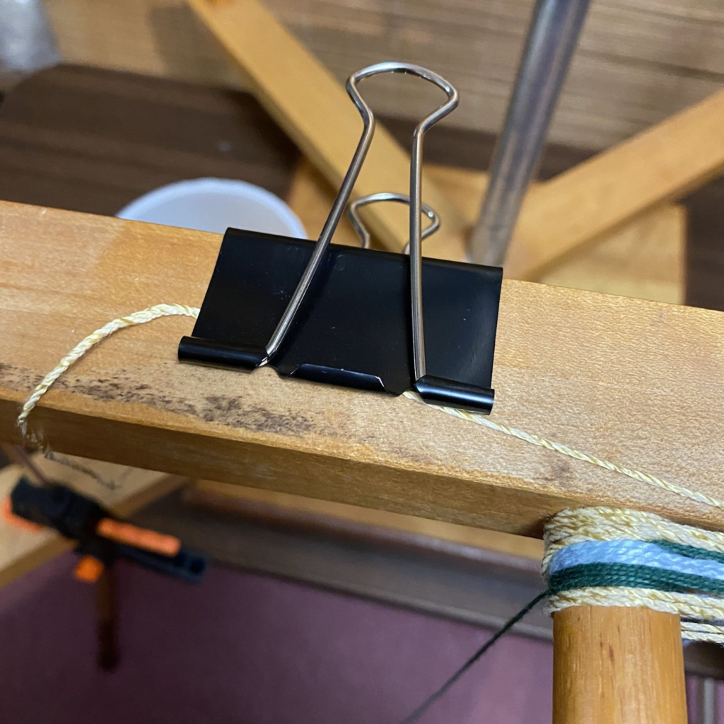 Photo of a binder clip attached to a warping mill to hold colors in waiting.